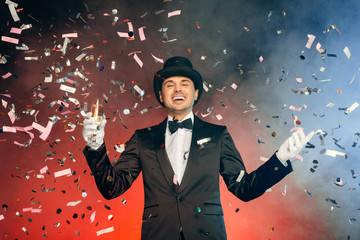 Professional Occupation. Showman in suit hat and gloves standing isolated on wall with flying confetti holding champagne laughing happy