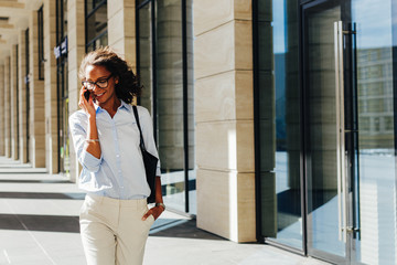 Woman walking at office building. Young entrepreneur talking on cell phone.