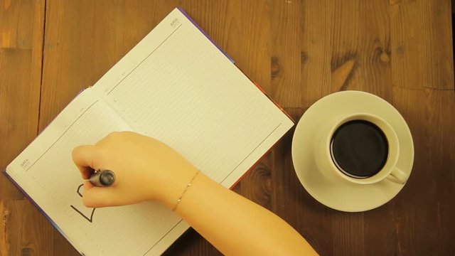 The girl writes in the diary the love word with a black marker and drinks coffee