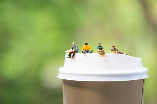 Miniatures people sitting on a cup of coffee using as background business concept.