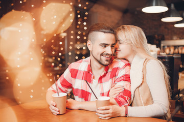 Beautiful lovers couple in cafeteria drink coffee to go, glare from garland foreground. Concept Valentine day