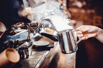 Barista whips milk with nozzle, strong jet of air steam coffee machine, holding pitcher in his hand