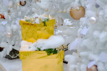 Golden box with a gift under the snow near the festive Christmas tree