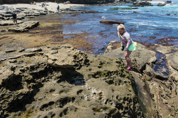 Blonde female explores the  rugged, rocky beach of La Jolla California during low tide