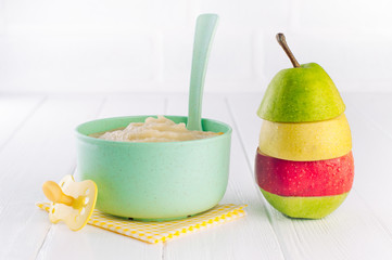 Fruit puree in bowl near pyramid of apples and pear pieces on white background