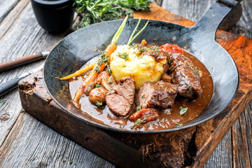 Traditionelle deutsche geschmorte Schweinebäckchen in brauner Rotwein Sauce mit Pilzen und Kartoffel Püree als closeup in einer schmiedeeisernen Pfanne