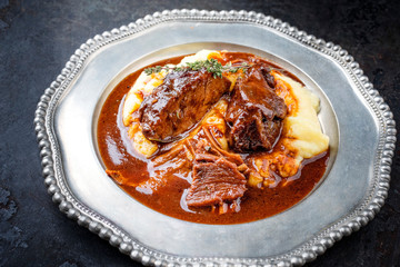 Traditionelle geschmorte Kalbsbäckchen in brauner Rotwein Sauce mit Kartoffel Püree als closeup auf einem Zinnteller