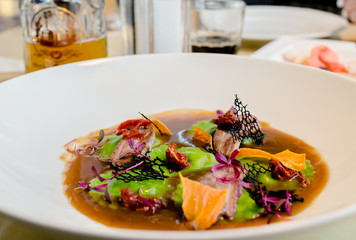 ravioli green in meat broth with pieces of seafood and dried tomatoes