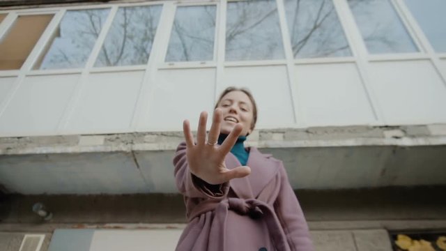 The girl in the lilac coat stands against the background of the old building and held out her hand. Hand in focus. On hand ring. The frame moves away from the girl (slow)