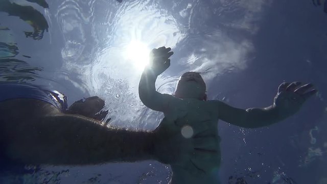 Happy smiling toddler is diving under water with father