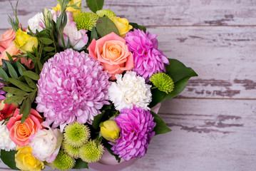 beautiful floral arrangement in the box, pink and yellow rose, pink eustoma, green and pink chrysanthemum, white carnation, dahlia on wooden background, top view, with space for text