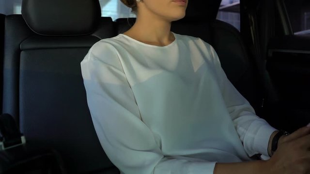 Nervous female looking at handwatch, sitting on car backseat hurrying to meeting
