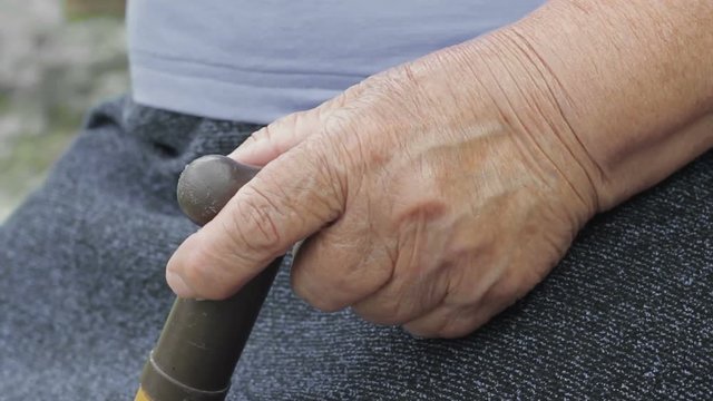 Exhausted, helpless granny sitting, having rest oudoors in garden, holding stike