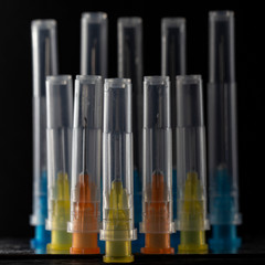 Medical needles with multi-colored heads in plastic covers from a syringe on a black background