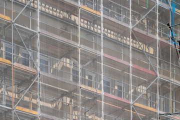 A scaffolding covered by netting attached to a building during refurbishment.