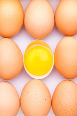 Brown organic eggs and one opened egg with egg yolk on a white background.