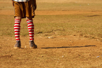 Fototapeta premium Lonely pair of feet of a young football goalie standing on a dusty cricket feet in Mumbai, India