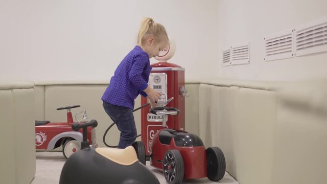 A little girl plays with beautiful stylish cars. She fills a toy car at a big red gas station. Early development of children. Game room for little car enthusiasts