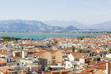 small south European harbor resort city with many houses with orange shingles roofs near harbor sea bay surrounded by mountain on horizon background 