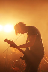 Silhouette of a guitarist of a rock band rocking on his electric guitar with floodlights in the background