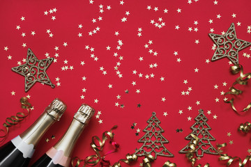 Two champagne bottles,Christmas ornaments and confetti stars on red background. Christmas...