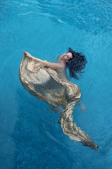 schöne dunkelhaarige Frau mit Locken relaxed in goldenen Tuch schwimmt glücklich schwebend im...