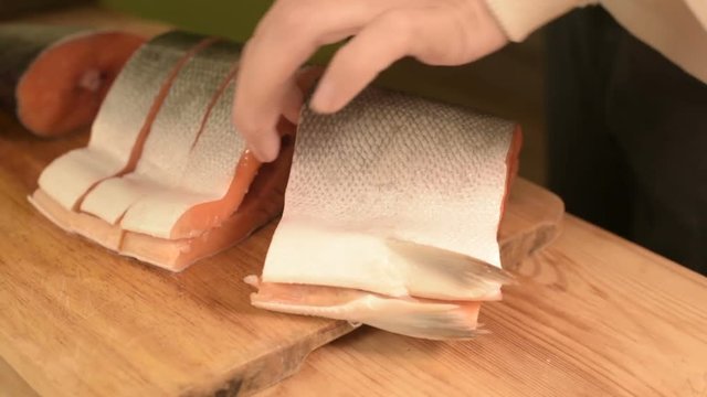 Close-up of female hands are cutting with a knife a large salmon on a wooden table of home cooking