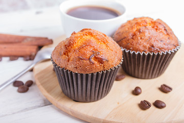 two carrot muffins with cup of coffee on wooden kitchen board on white wooden background