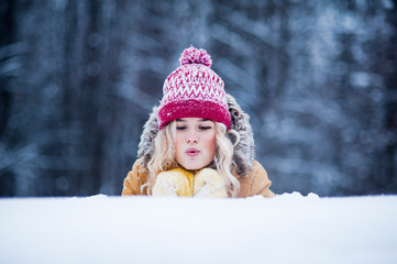 Very beautiful bright young girl in a red hat and yellow mittens on the background of a winter park in the snow. Winter holidays concept.