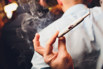 IQOS heat-not-burn tobacco product technology. Man holding e-cigarette in his hand before smoking.