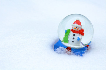 Glass ball with a snowman inside in the snow. Close-up. Background. Texture.