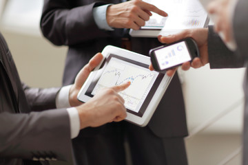 Businessmen at meeting presenting charts on smartphone, tablet