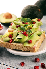 sliced avocado and ripe pomegranates on toast bread with spices and avocado.