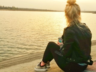  photo of a girl by the sea, looking into the distance, a bright landscape with a girl, a girl sitting near the sea from a hill, a stylish girl in nature, a beautiful haircut, a bright woman