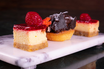 Set of mini cakes in assortment on white plate. Restaurant menu. Blackberry cake with raspberries. Tartlet with fruits. Close up.