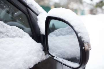 Car's side view mirror of a modern car covered  with snow