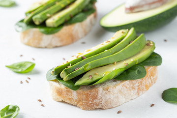 Two ciabatta toast with sliced avocado olive oil, spinach and flax and sesame seeds. Healthy vegetarian Breakfast on white background