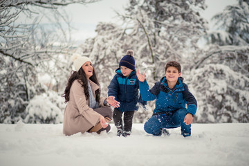 Fototapeta na wymiar Beautiful mom throwing around snow with her cute, little boys, enoying winter