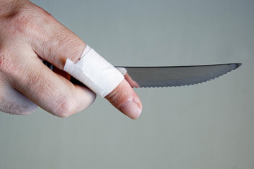 A knife with notches in the hand of a man with a wounded finger. On a light background