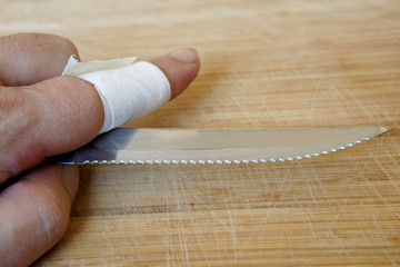 A sharp knife with notches in the hand of a man with a wounded finger. Against the background of a...