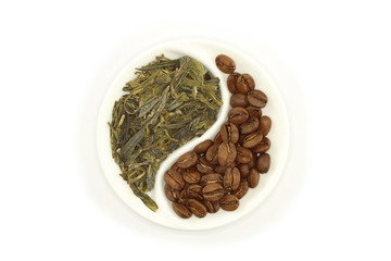 Green tea and roasted coffee beans in round Yin and Yang saucer on white background