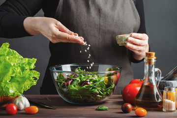 Woman chef in the kitchen preparing vegetable salad. Healthy Eating. Diet Concept. A Healthy Way Of Life. To Cook At Home. For Cooking. The girl sprinkles salt in a salad on a dark background