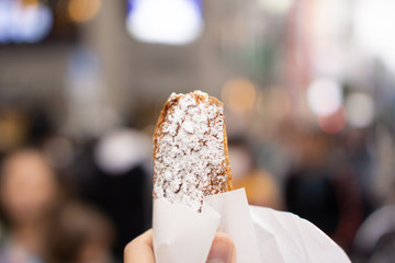 Tourist’s hand holding snack while walking in crowded street (day time)