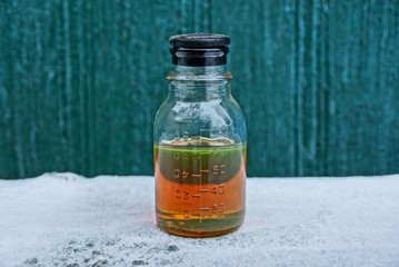 one closed brown liquid from engine oil in a glass bottle on white snow on a green background
