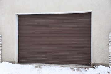 one brown closed gate on the front of a garage outside in the snow