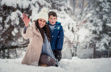 Fototapeta na wymiar Beatiful mom enjoying winter with her cute, little son, throwing snowballs