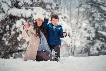 Beatiful mom enjoying winter with her cute, little son, throwing snowballs