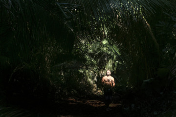 Young man in the green pacific jungle looking at sun lighting his face 