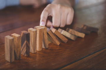  Businessman hand stopping falling wooden dominoes effect from continuous toppled or risk, strategy...