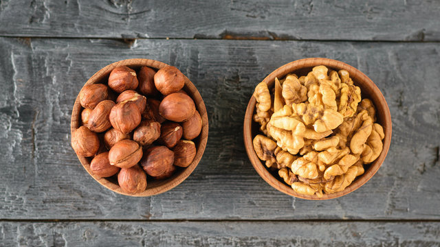 Wooden bowl with hazelnuts and wallnuts on a black rustic table. The view from the top.